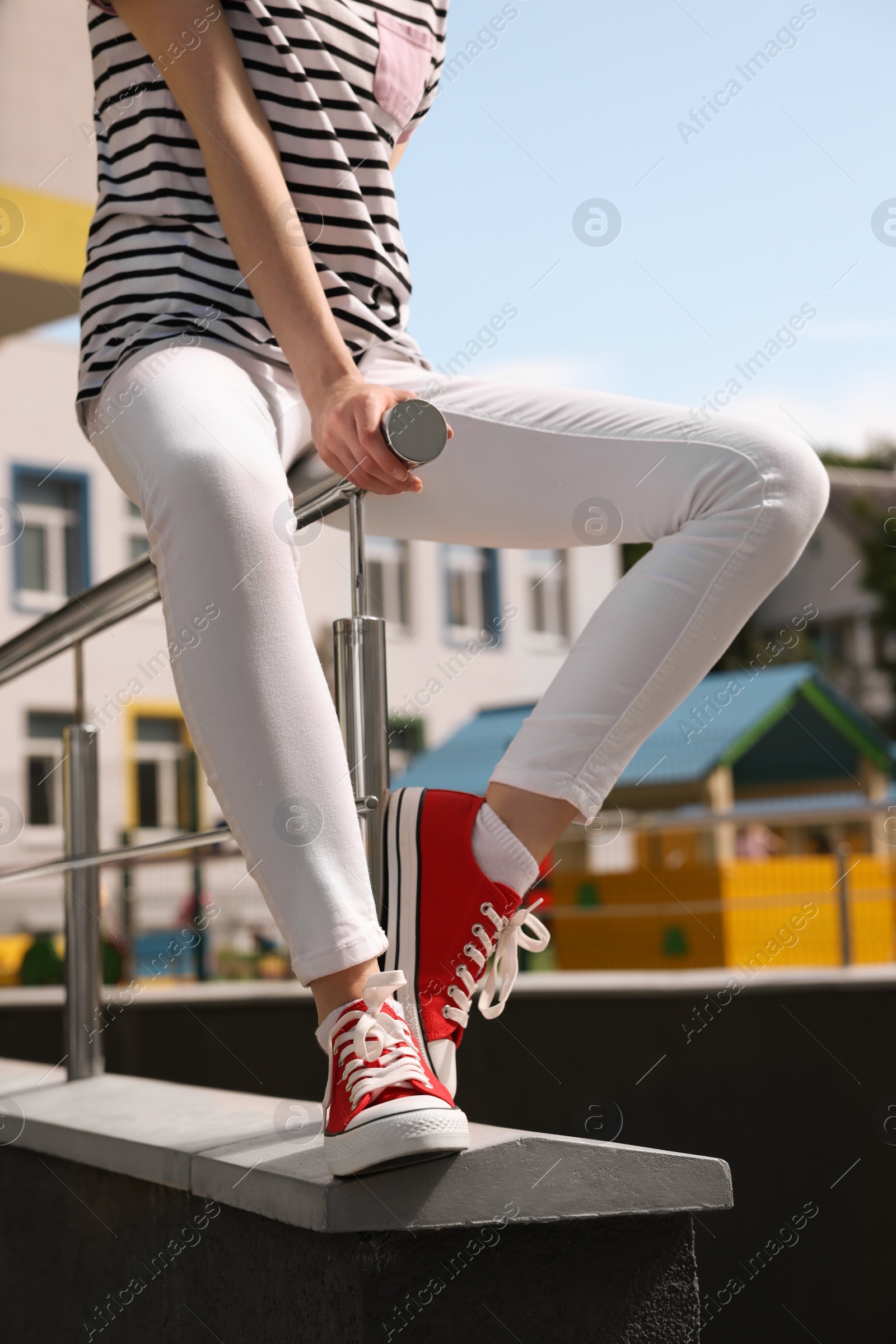 Photo of Woman in red classic old school sneakers sitting on railing outdoors, closeup