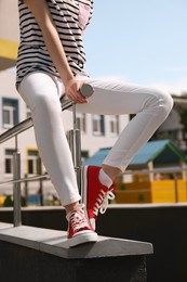 Photo of Woman in red classic old school sneakers sitting on railing outdoors, closeup