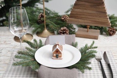 Festive place setting with beautiful dishware, cutlery and gingerbread house card holder for Christmas dinner on white wooden table