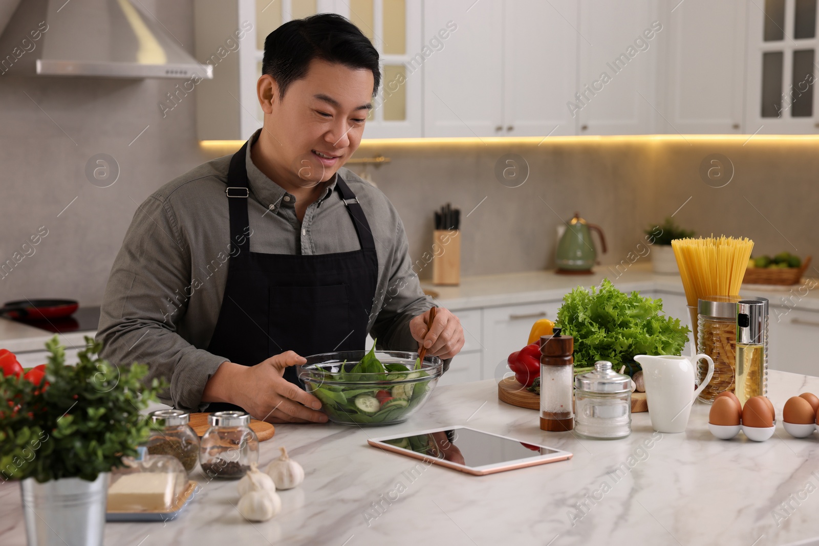 Photo of Man using tablet while cooking in kitchen