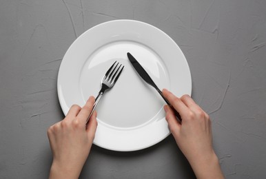 Photo of Woman with empty plate and cutlery at grey textured table, top view