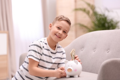 Photo of Little boy with piggy bank and money at home