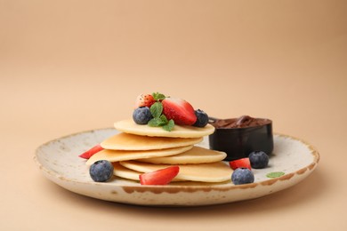 Delicious pancakes served with berries and chocolate spread on beige background, closeup