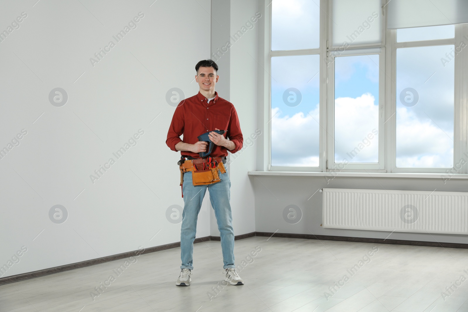 Photo of Handyman with electric screwdriver and tool belt in empty room