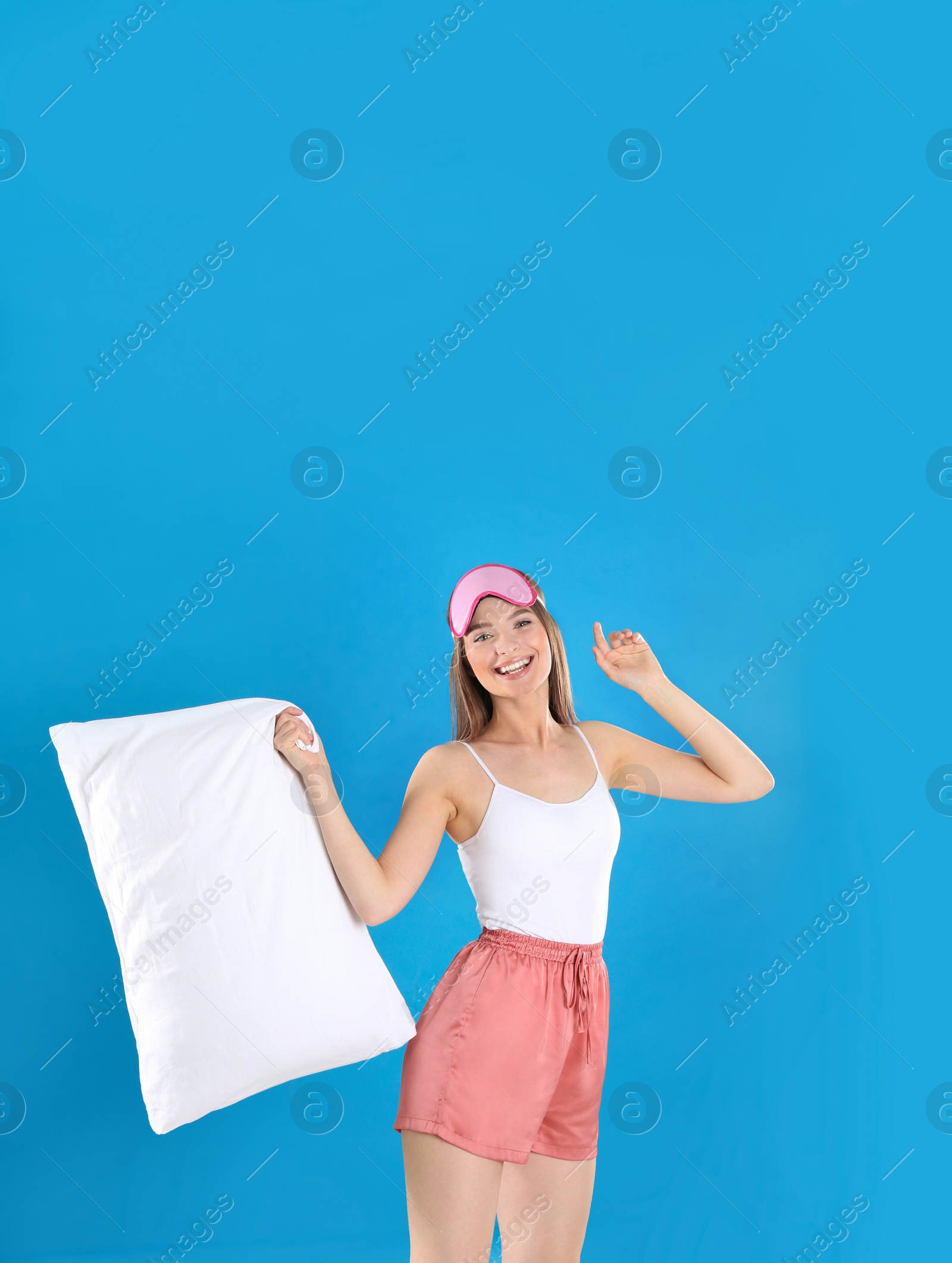 Photo of Young woman with pillow and sleep mask on blue background