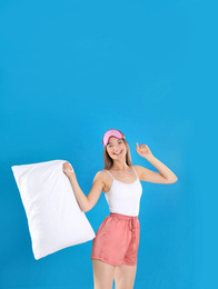 Young woman with pillow and sleep mask on blue background