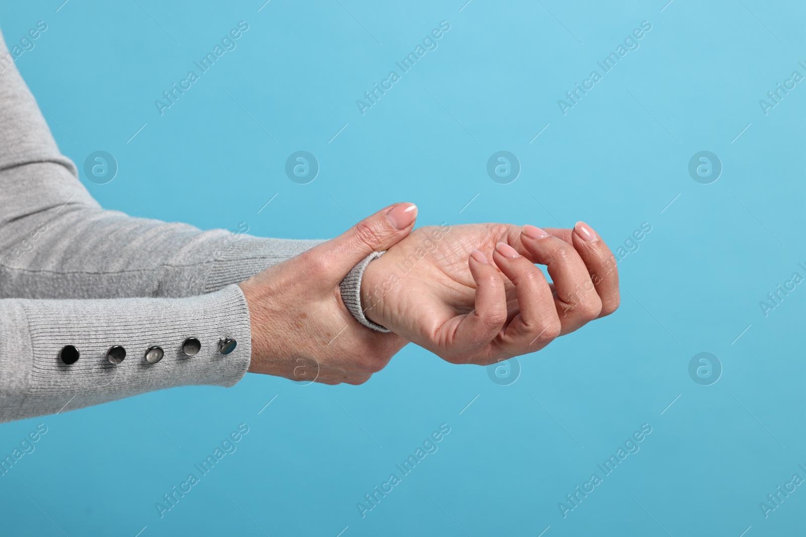 Photo of Arthritis symptoms. Woman suffering from pain in wrist on light blue background, closeup