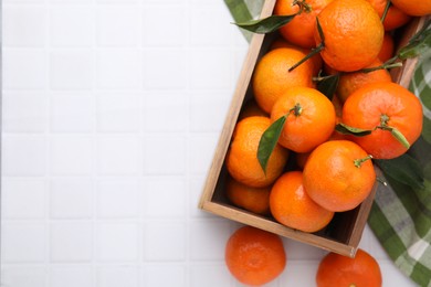 Photo of Wooden crate with fresh ripe tangerines and leaves on white tiled table, top view. Space for text