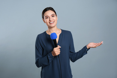 Young female journalist with microphone on grey background