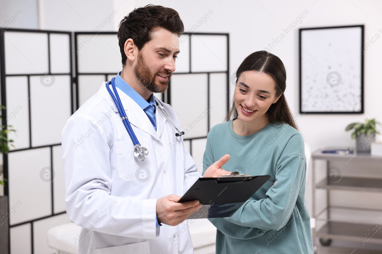 Photo of Doctor with clipboard consulting patient during appointment in clinic