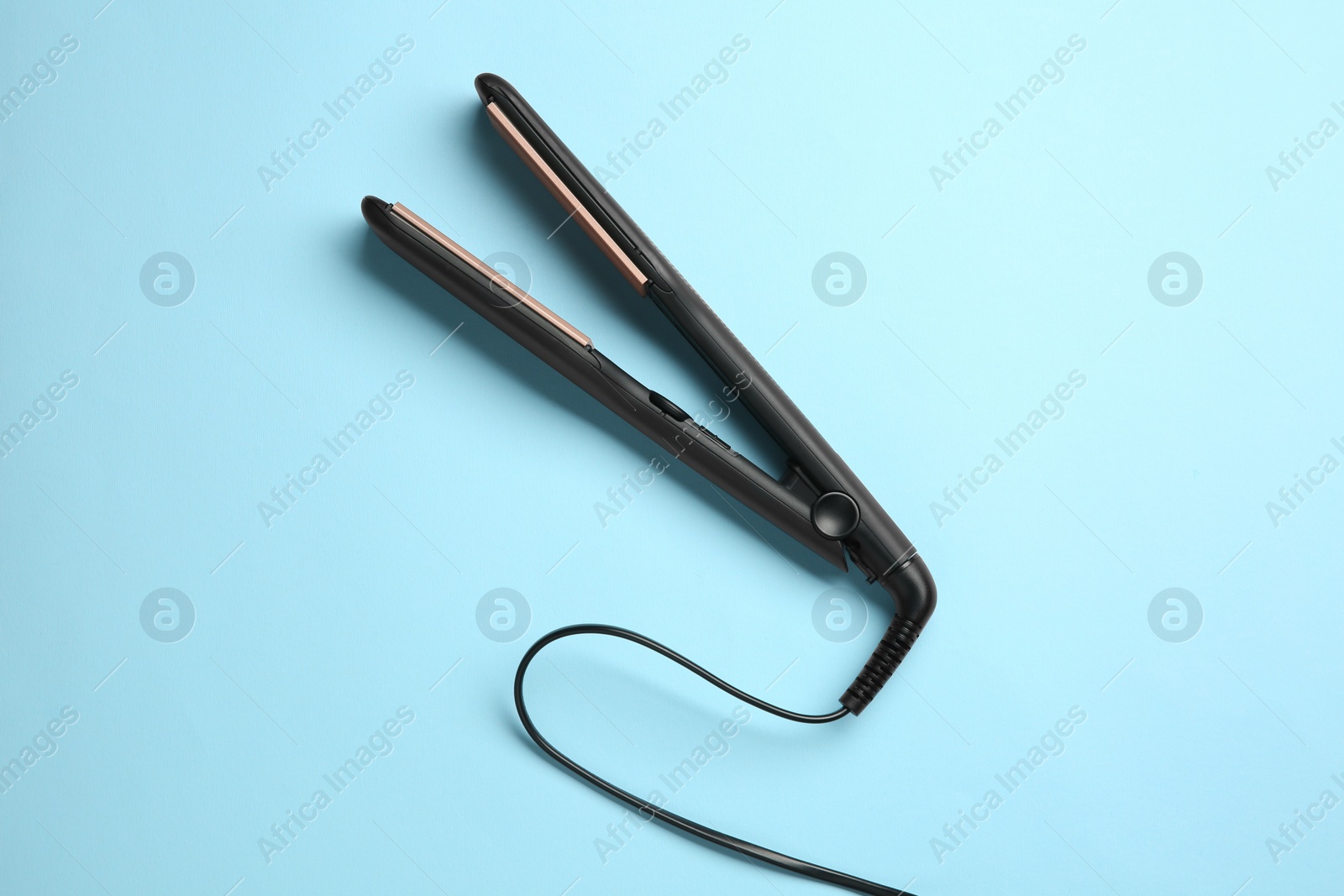 Photo of Modern flat hair iron on light blue background, top view