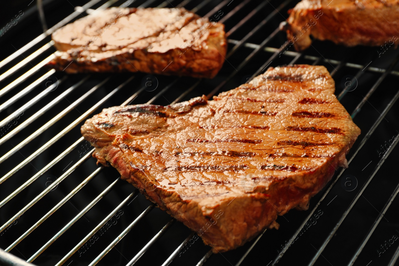 Photo of Fresh grilled tasty meat steaks on barbecue grate, closeup