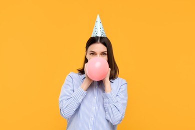 Photo of Young woman in party hat blowing balloon on yellow background