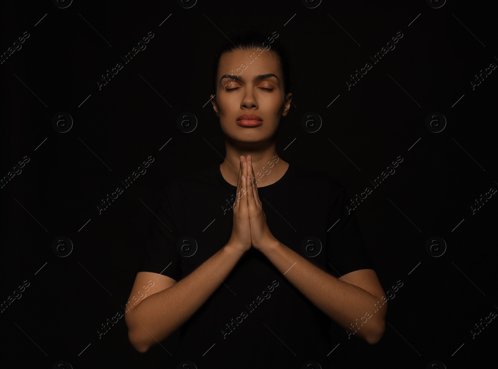 Photo of African American woman with clasped hands praying to God on black background