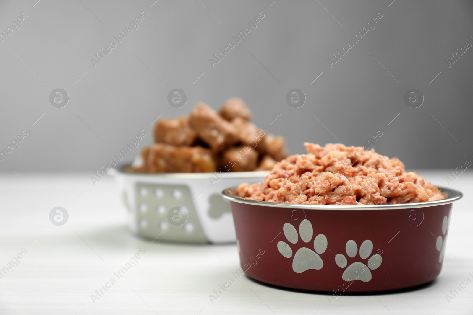 Photo of Wet pet food in feeding bowl on white table, space for text