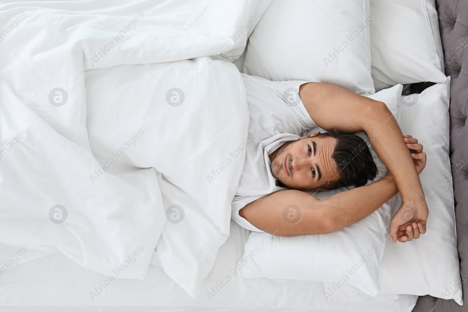 Photo of Young man lying in bed with soft pillows at home, top view