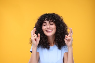Woman crossing her fingers on yellow background