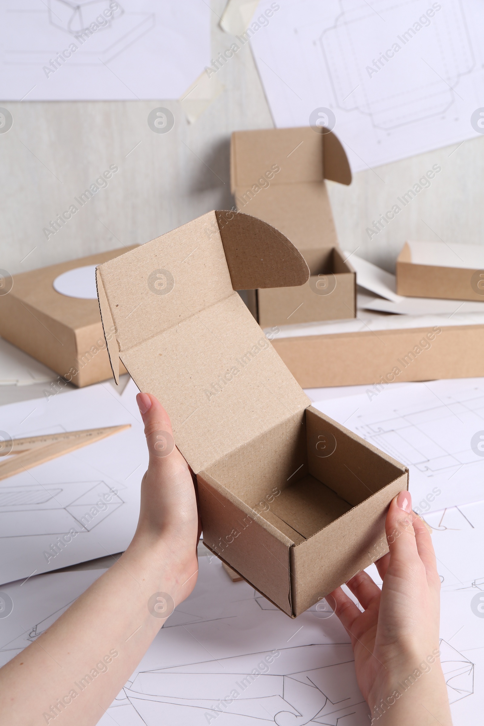 Photo of Woman holding cardboard box near drawings at table, closeup