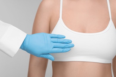 Mammologist checking woman's breast on light grey background, closeup