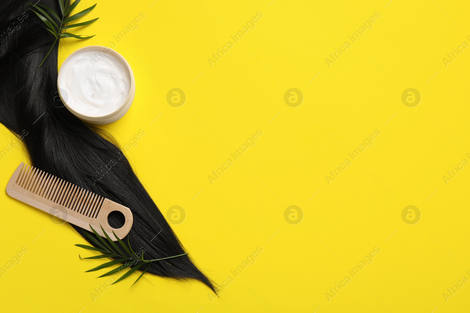 Photo of Lock of healthy black hair, cosmetic product and comb on yellow background, flat lay. Space for text