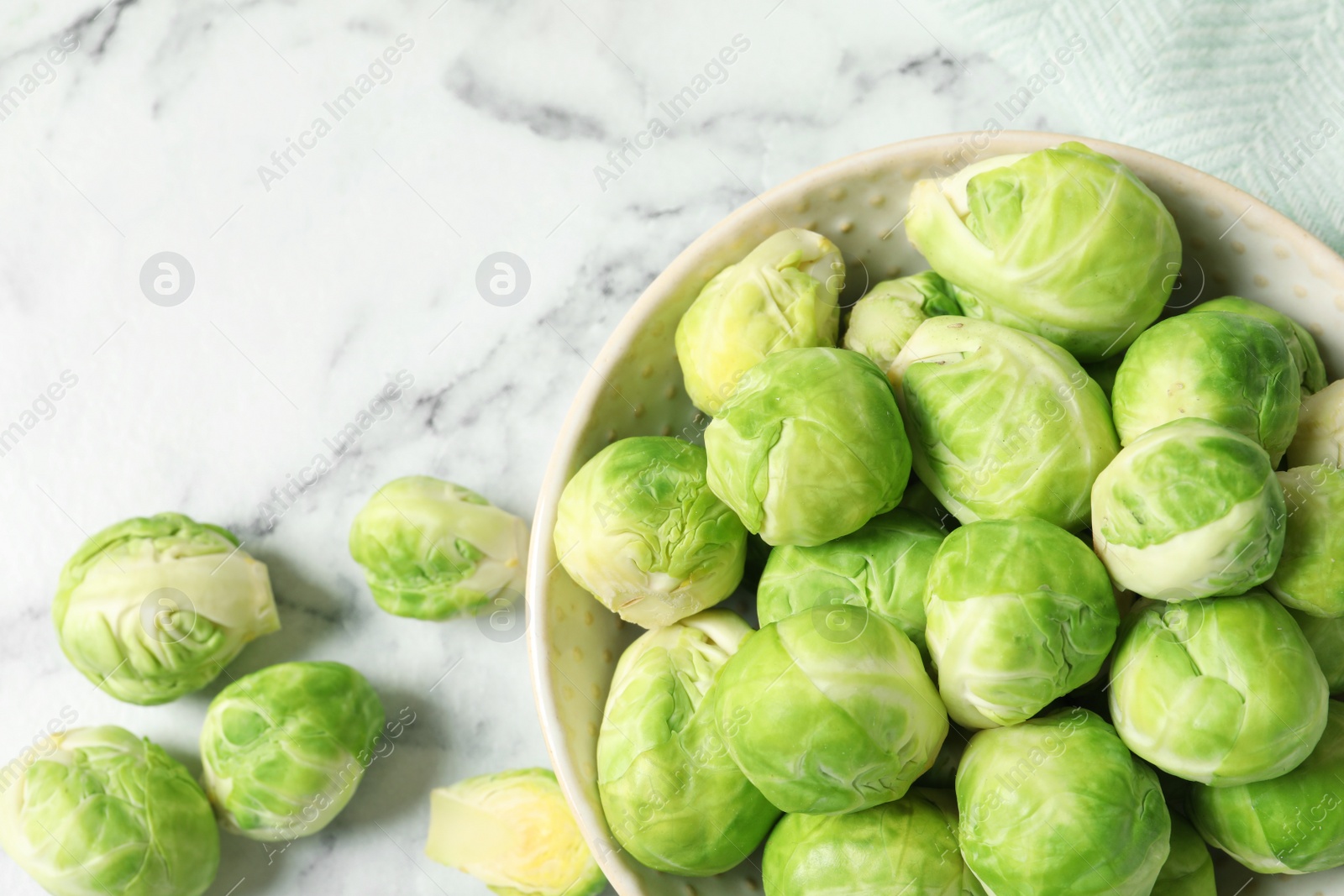 Photo of Bowl with fresh Brussels sprouts on marble table, top view. Space for text