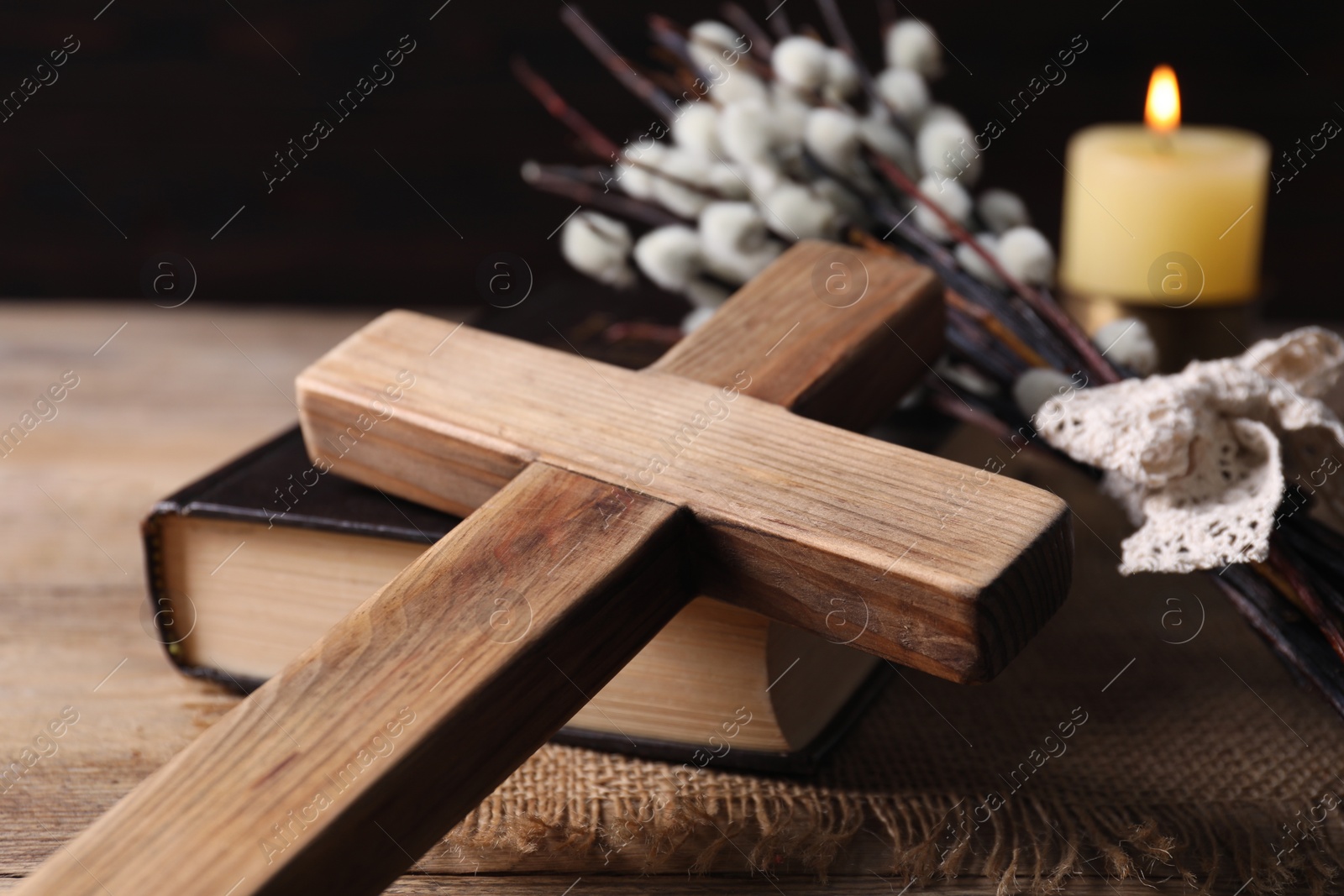 Photo of Cross, Bible, burning church candle and willow branches on wooden table, closeup