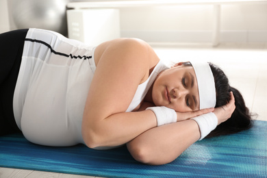 Lazy overweight woman sleeping instead of training on mat at gym