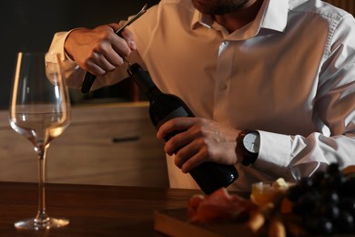 Romantic dinner. Man opening wine bottle with corkscrew at table indoors, closeup