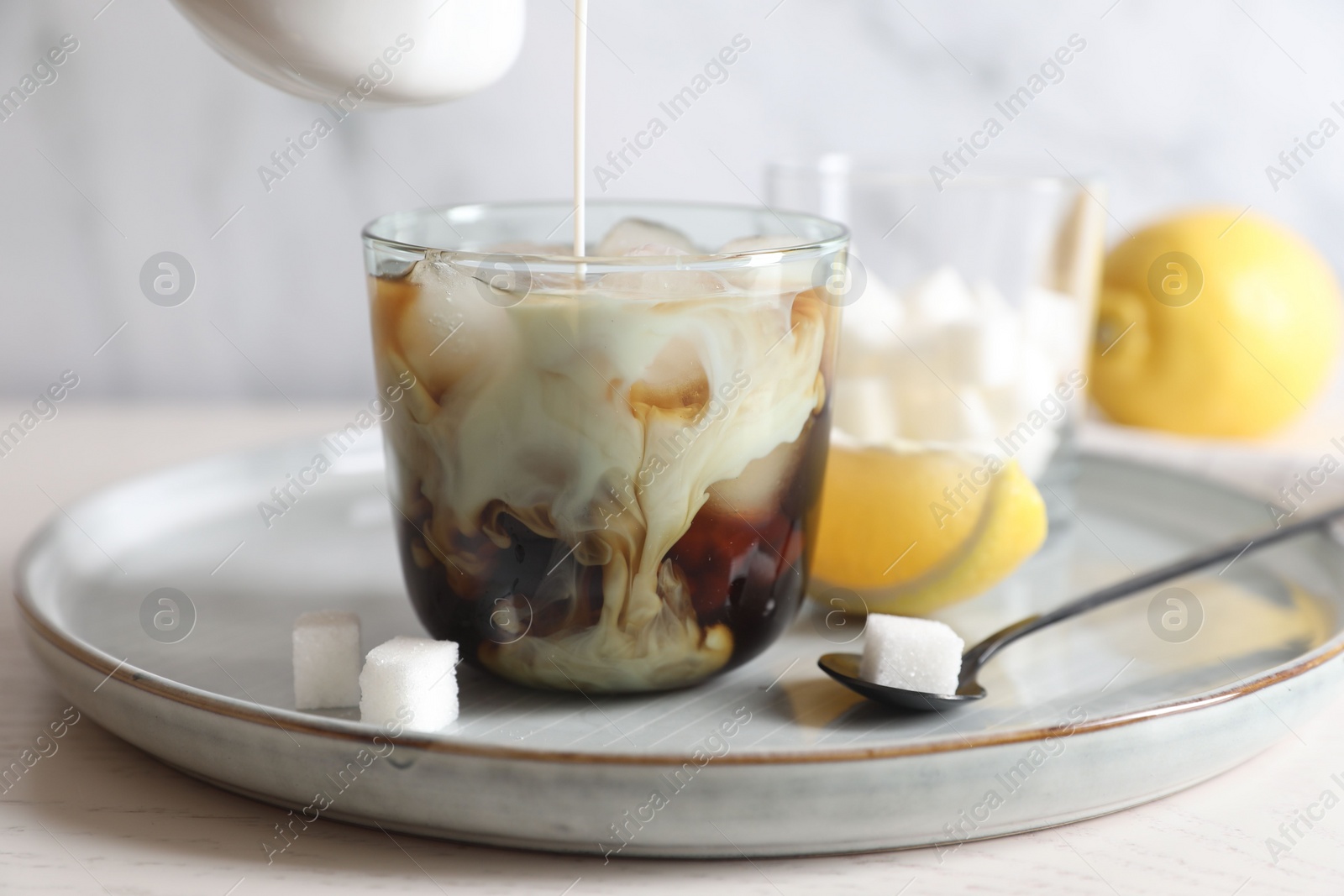 Photo of Pouring milk into glass with refreshing iced coffee at white wooden table, closeup