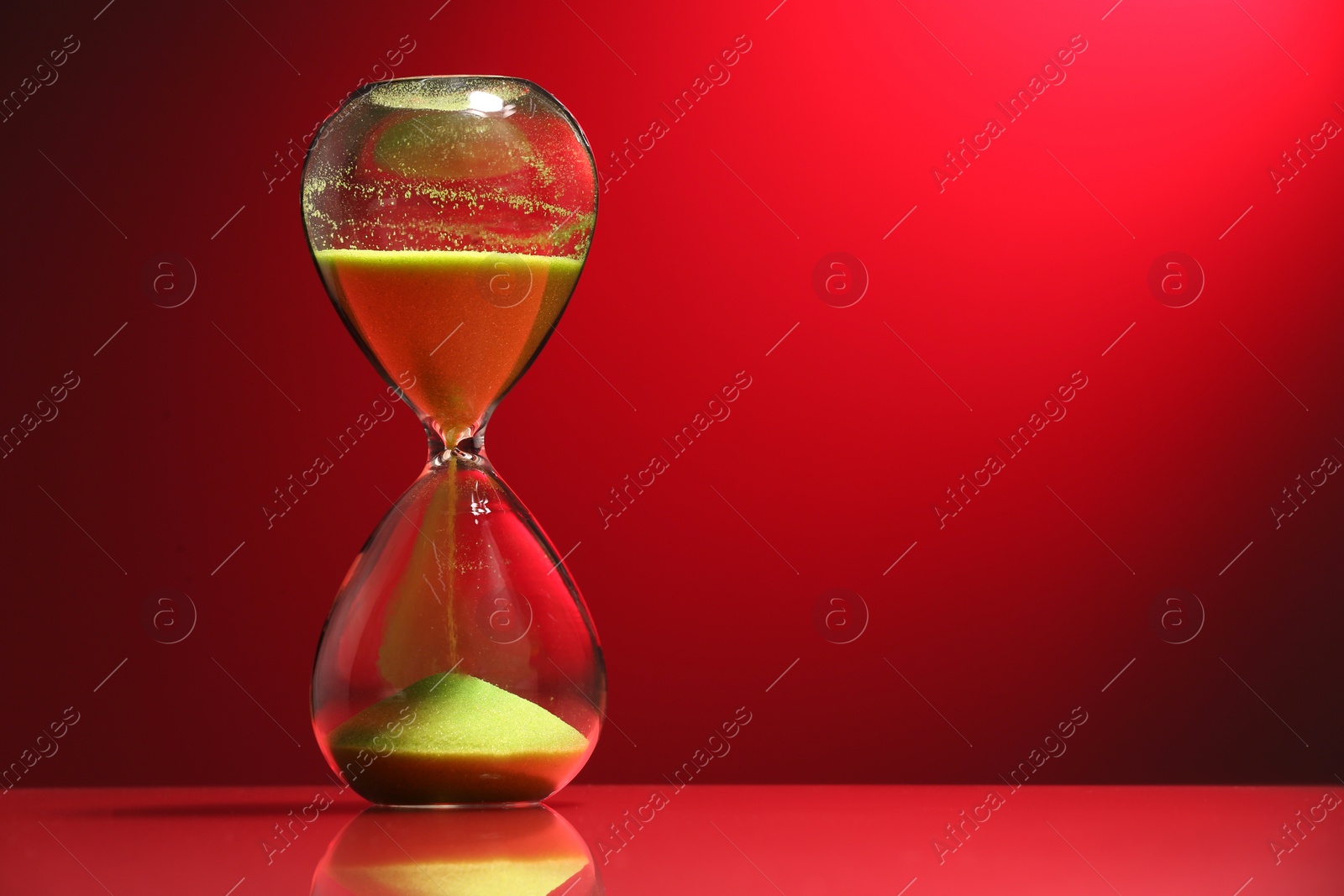 Photo of Hourglass with yellow flowing sand on red background. Space for text