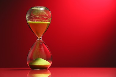 Photo of Hourglass with yellow flowing sand on red background. Space for text