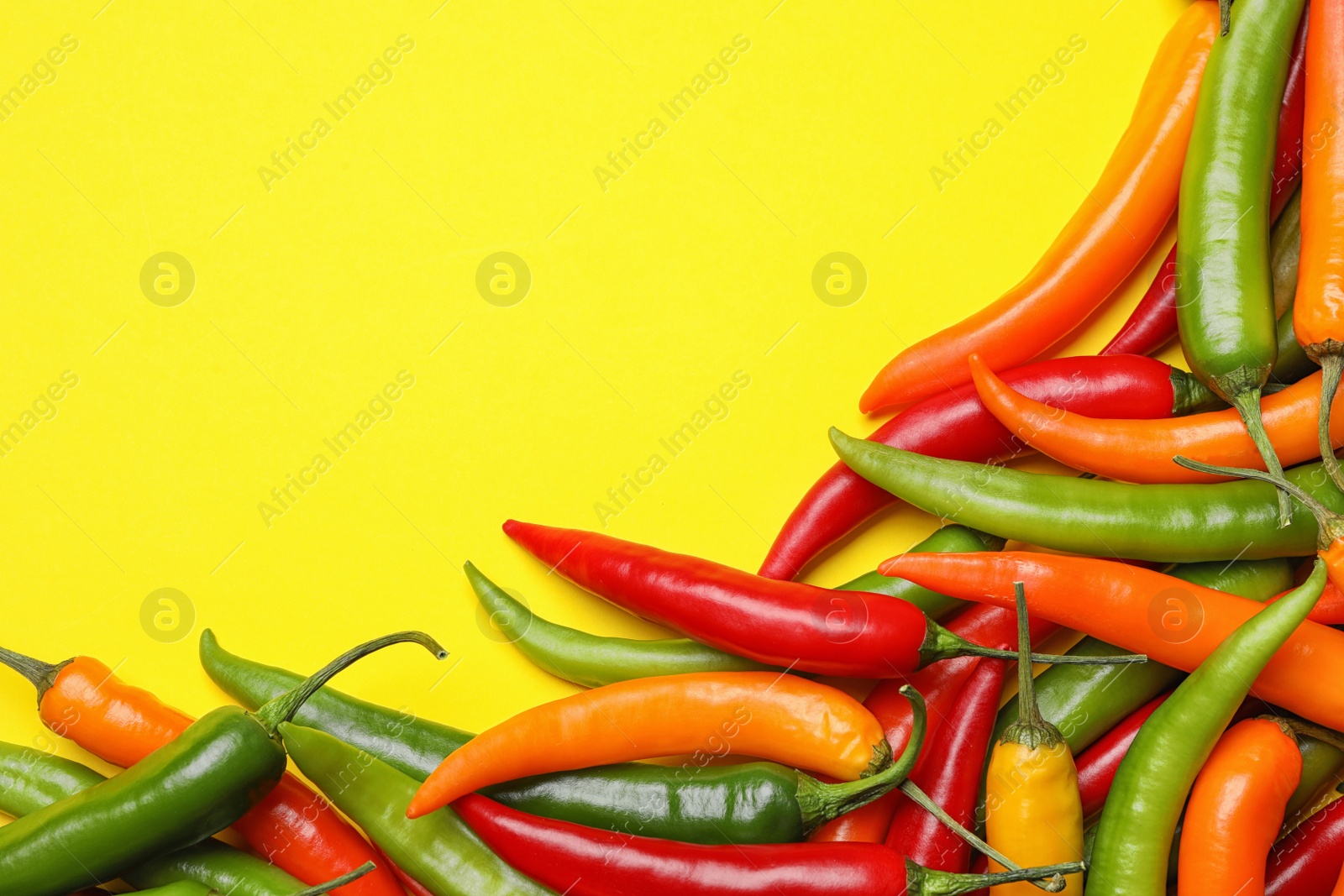 Photo of Different hot chili peppers on yellow background, flat lay. Space for text
