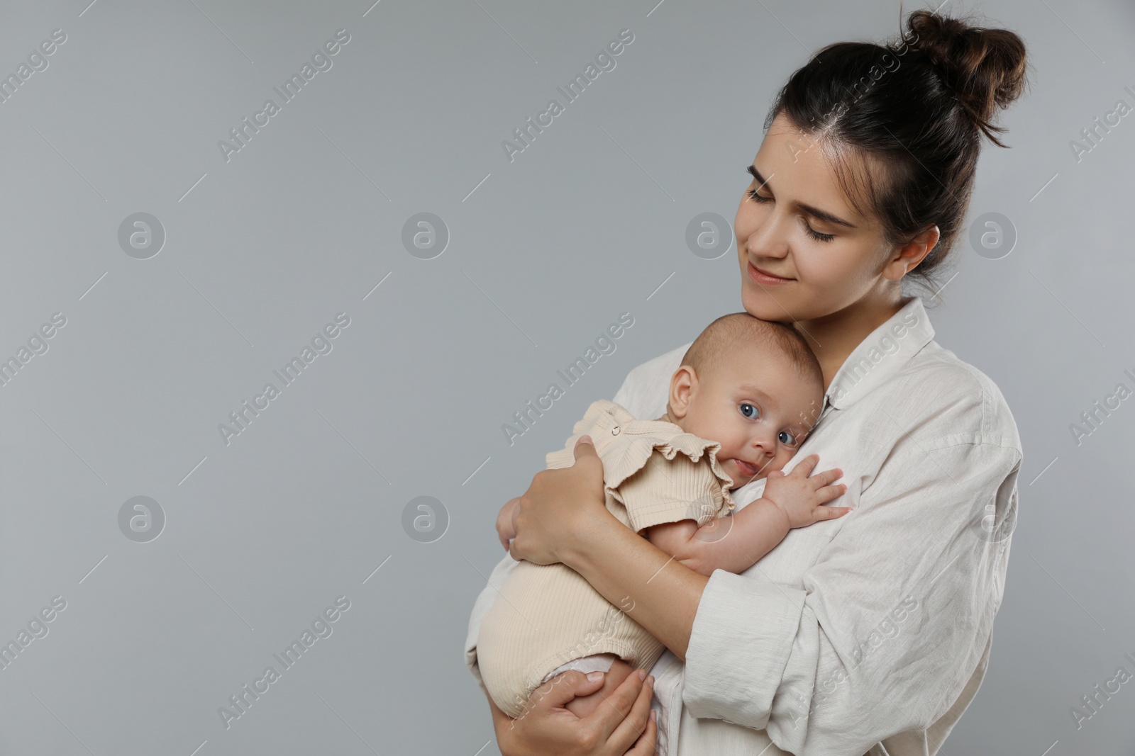 Photo of Beautiful mother with her cute baby on grey background. Space for text