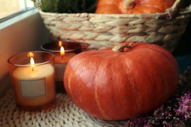 Photo of Wicker basket with beautiful heather flowers, pumpkins and burning candles near window indoors, closeup
