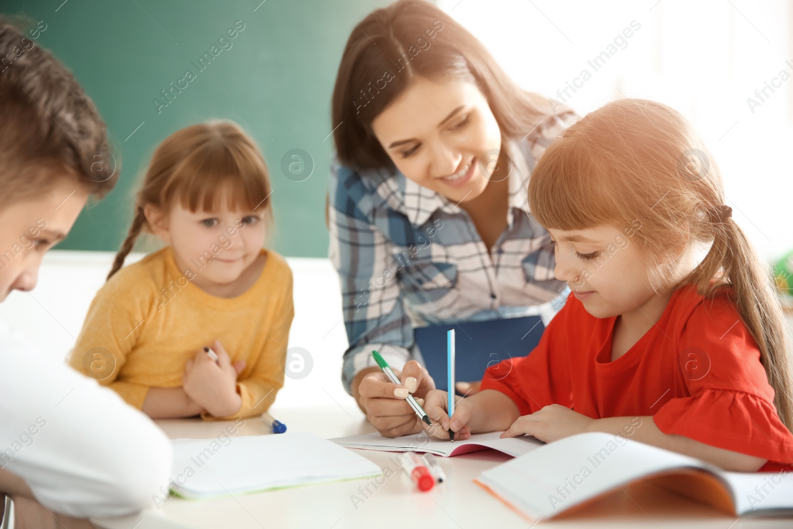 Photo of Female teacher helping girl with her task in classroom at school