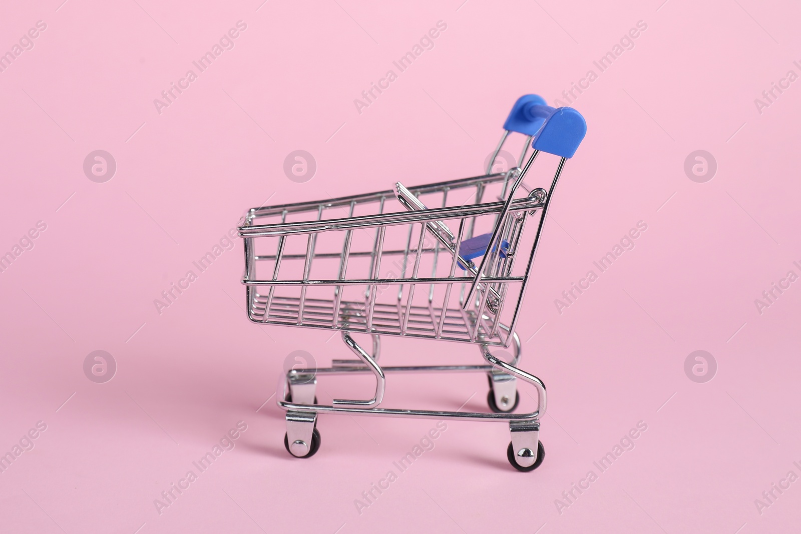 Photo of Small metal shopping cart on pink background