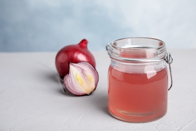 Photo of Glass jar with onion syrup and fresh vegetable on table. Space for text