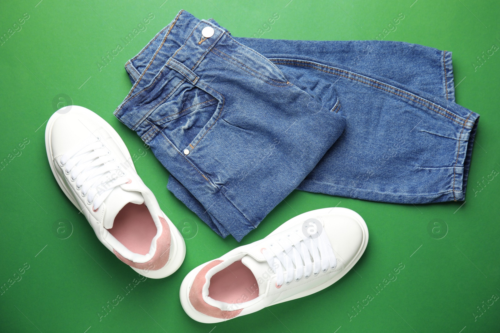 Photo of Stylish white sneakers and jeans on green background, flat lay