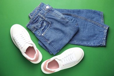 Photo of Stylish white sneakers and jeans on green background, flat lay