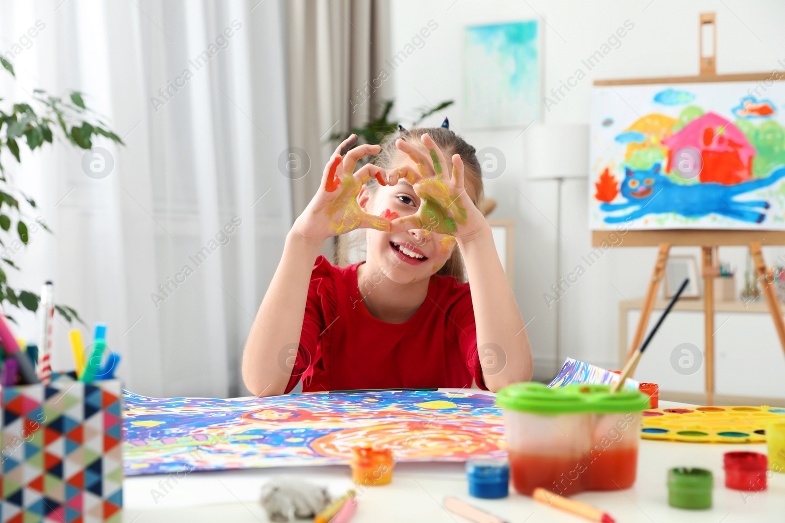 Photo of Little child making heart with painted hands at table indoors