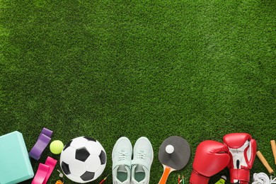 Different sport equipment and sneakers on green grass, flat lay. Space for text