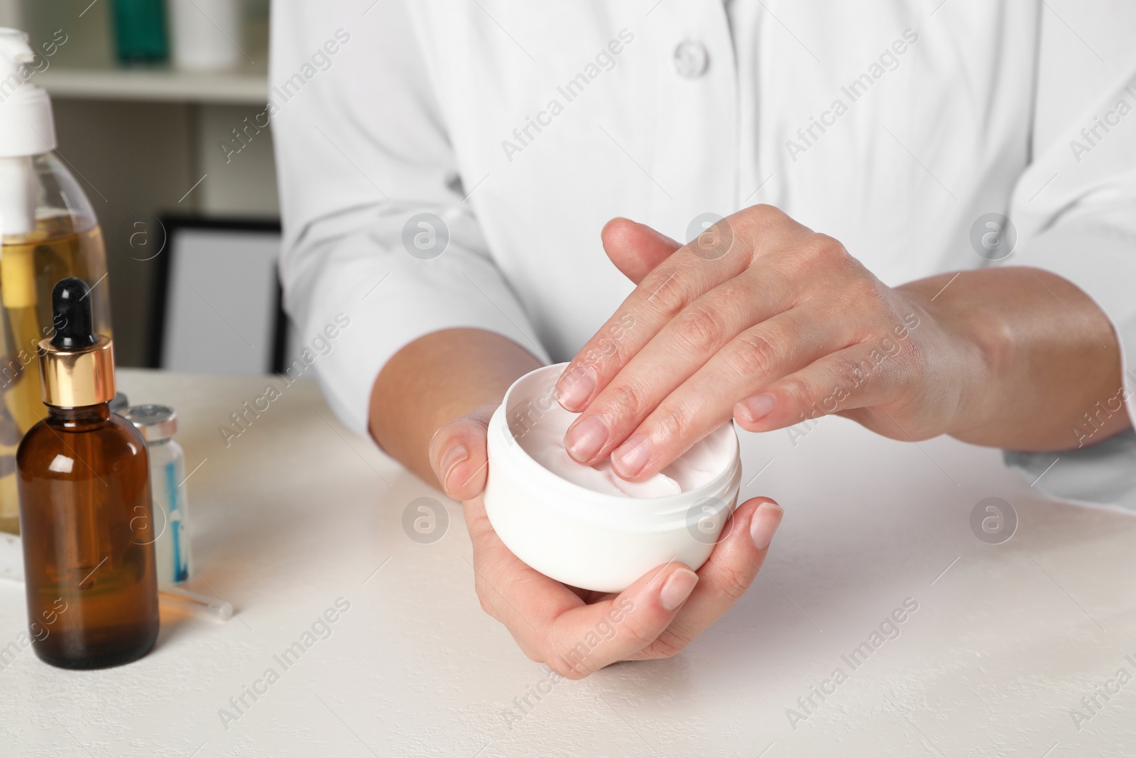 Photo of Dermatologist testing cosmetic product at white table indoors, closeup