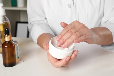 Photo of Dermatologist testing cosmetic product at white table indoors, closeup