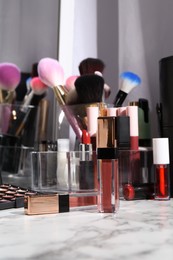 Bright lip glosses among different cosmetic products on white dressing table