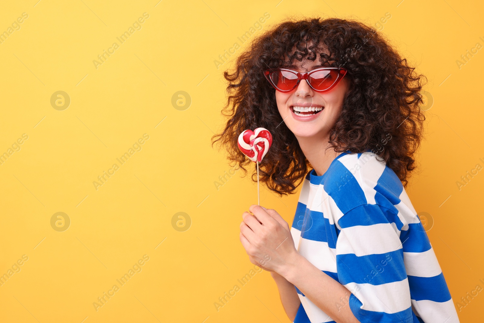 Photo of Beautiful woman in sunglasses with lollipop on yellow background, space for text