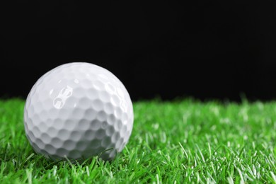 Golf ball on green grass against black background, closeup. Space for text