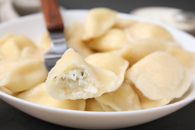 Photo of Delicious dumpling (varenyk) with cottage cheese on fork over bowl, closeup