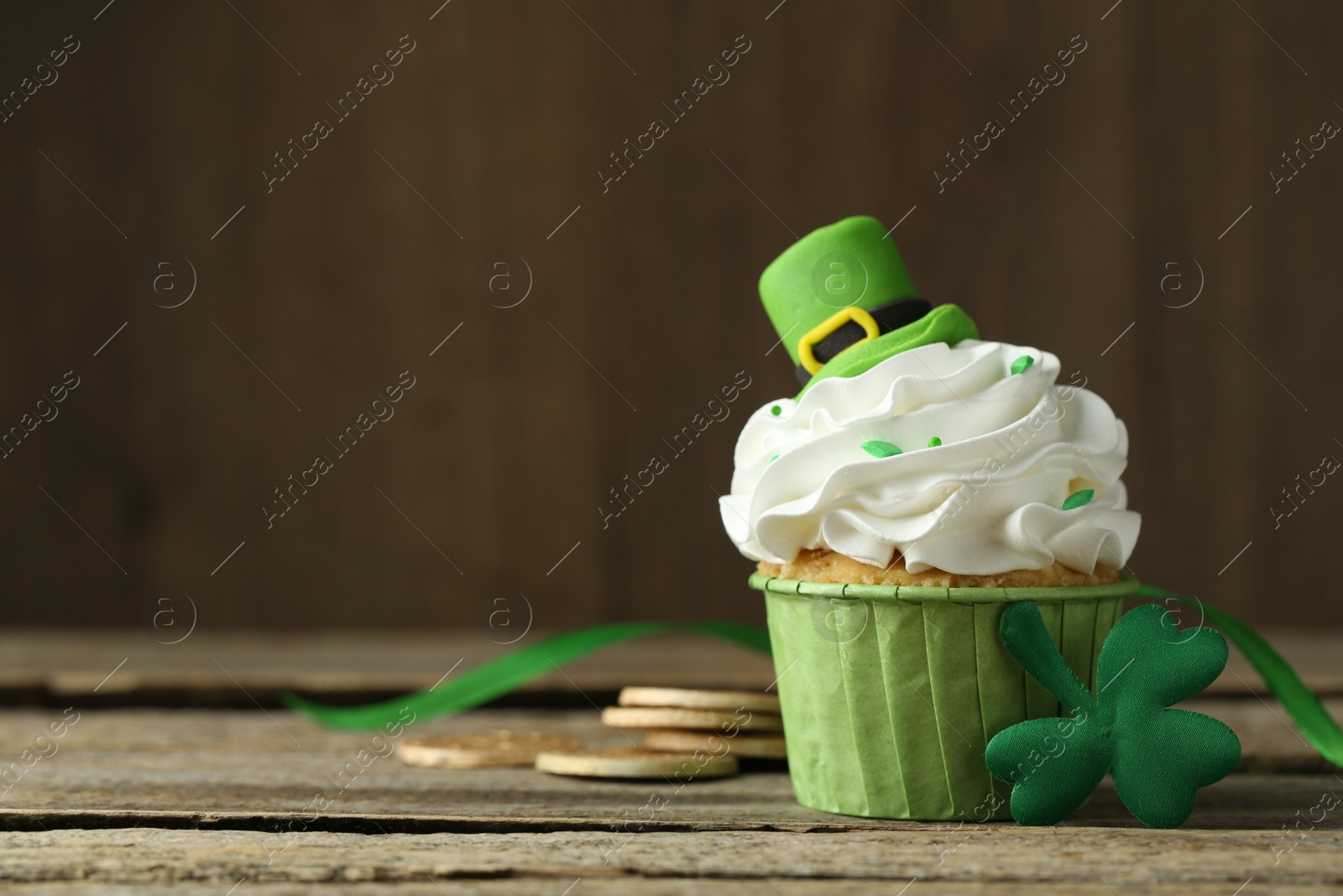 Photo of St. Patrick's day party. Tasty cupcake with green leprechaun hat topper on wooden table, closeup. Space for text