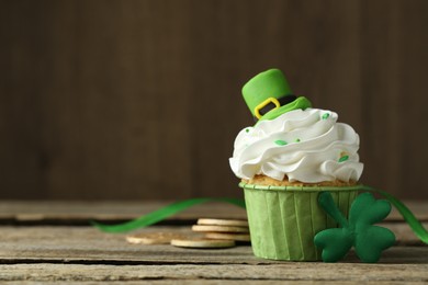 Photo of St. Patrick's day party. Tasty cupcake with green leprechaun hat topper on wooden table, closeup. Space for text