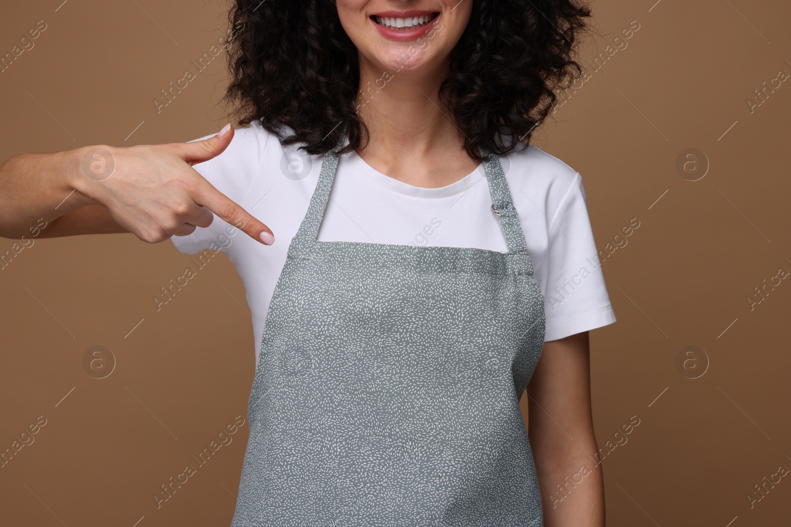 Photo of Woman pointing at kitchen apron on brown background, closeup. Mockup for design